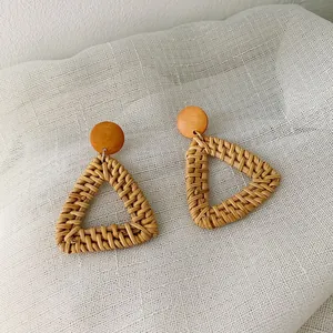 Detailed view of bohemian triangular woven rattan earrings with natural wood studs