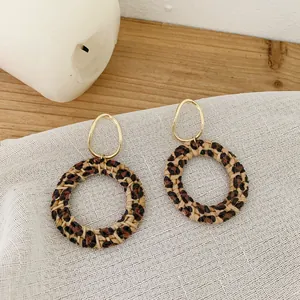 Bohemian rattan hoop earrings with leopard print and golden oval studs on wood background