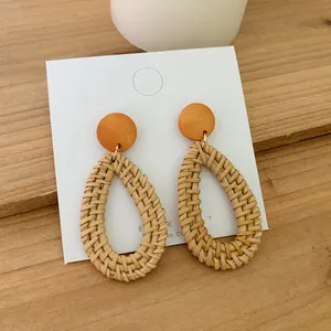 Macro detail of Bohemian woven rattan teardrop earrings on a wooden surface with a white card