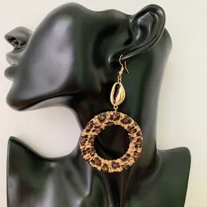 Detail of bohemian rattan hoop earring with gold seashell stud on a dark model