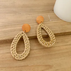 Detail of woven rattan teardrop earrings with orange wood accent on a rustic background