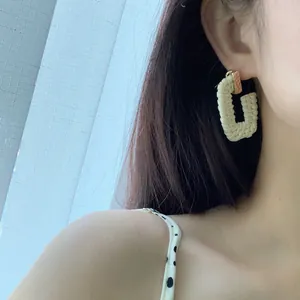 Bohemian cream woven rectangular hoop earrings with gold studs worn by a model