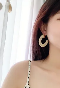 Detail of bohemian raffia woven hoop earring with gold metal stud worn by a model