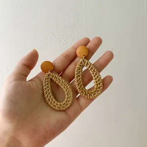 Detail of handmade woven rattan teardrop earrings with a yellow wood stud for women