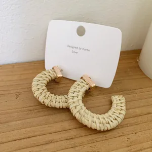 Detail of cream woven C-shape rattan earrings with textured gold metal and S925 silver stud