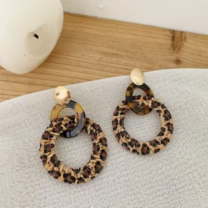 Close-up of leopard print straw earrings with golden studs on a rustic wood background