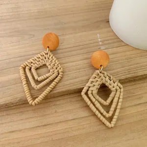 Detailed view of handmade geometric rattan drop earrings with wooden stud on timber background