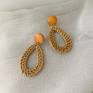 Close-up of handmade woven rattan teardrop earrings with natural wood stud and gold hardware