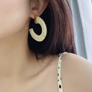 Close-up of C-shaped woven rattan earrings in beige on model showing natural texture