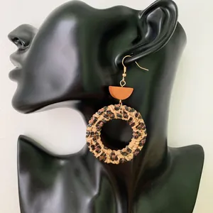 Detail of round leopard print wicker earrings on a black model silhouette with gold hooks