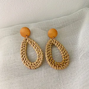 Close-up of bohemian handmade woven rattan teardrop earrings with orange wooden studs