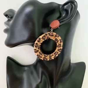 Detail of bohemian leopard print woven rattan hoop earrings on a black model