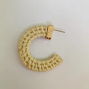 Close-up of bohemian C-shaped woven rattan earrings with textured gold metal studs