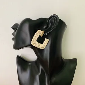 Handmade bohemian square rattan earrings with golden metal accents on model