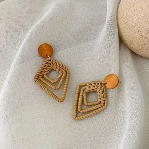 Close-up of geometric rattan earrings with round wooden studs on white linen fabric