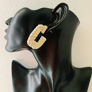 Close-up of bohemian cream woven rattan C-hoop earrings on a black mannequin display