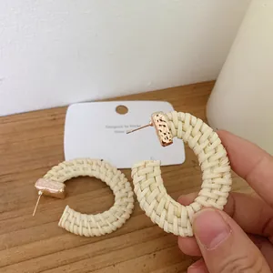 Handheld view of woven C-shape hoop earrings with hammered rose gold metal tips