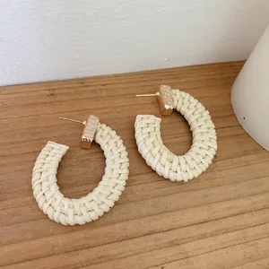 Detail of handmade C-shape rattan woven earrings with hammered gold metal studs