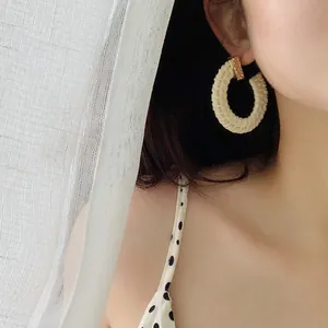 Close-up of handmade bohemian woven straw earrings on model for summer beach look
