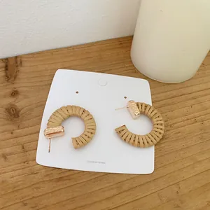 Detail view of Bohemian C-shape woven rattan hoop earrings on a wooden background