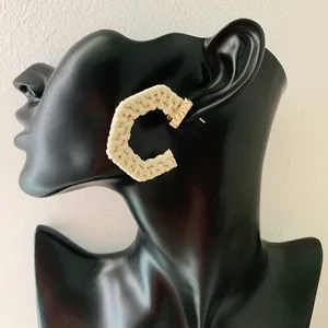 Detailed close-up of C-shaped woven rattan hoop earrings with gold metal accents