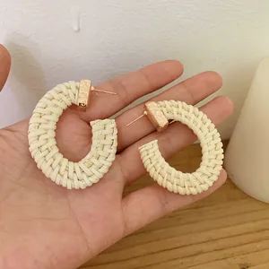 Detail of handmade bohemian woven rattan C-shape hoop earrings held in hand