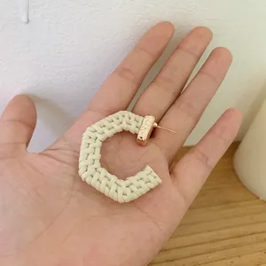 Detail of C-shaped woven rattan earring with wavy gold-plated textured metal stud