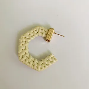 Close-up of C-shaped beige woven rattan earring with textured gold metal fastener