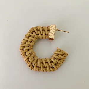Detail of C-shaped woven rattan earring with hammered gold metal accents for women