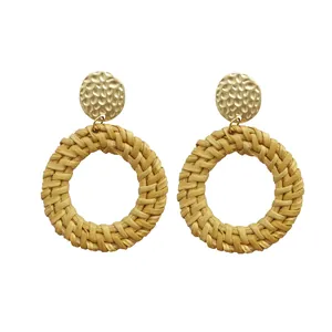 Detail of bohemian rattan drop earrings featuring textured gold metal discs and woven circles