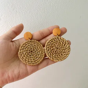 Close-up of handmade Bohemian round rattan earrings with orange wood accents