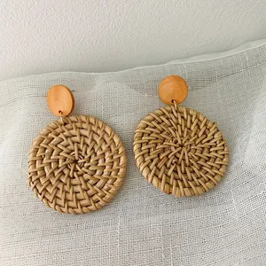 Detail of bohemian handmade woven rattan drop earrings on textured gray linen background