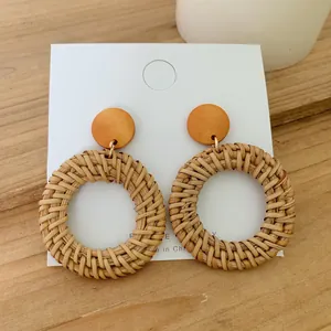 Close-up of Bohemian rattan woven earrings on a white card against a wooden background
