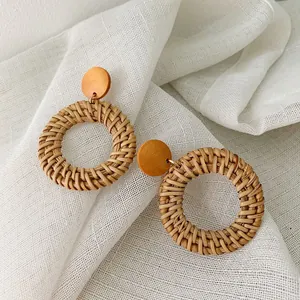 Macro detail of hand-woven rattan hoop earrings with natural wooden studs on fabric