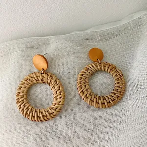 Close-up of handmade rattan hoop earrings with brown wooden discs on linen fabric