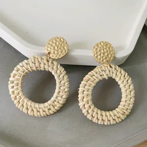 Close-up of bohemian wicker drop earrings featuring golden hammered metal studs and woven rings