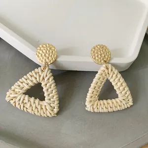 Detailed shot of bohemian beige rattan woven triangle earrings with gold hammered metal studs