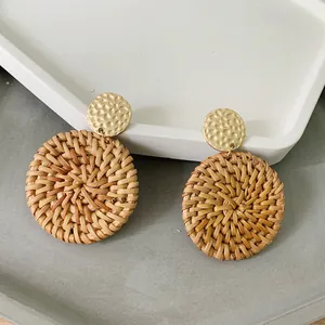 Close-up of bohemian rattan earrings with hammered gold metal disc and woven texture