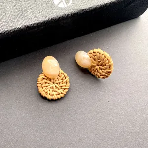 Detailopname van gevlochten rotan oorbellen met beige marmeren hars details