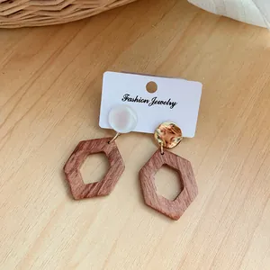 Detalle de pendientes asimétricos de madera con colgante hexagonal y detalles mixtos