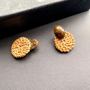 Detailopname van geweven strooien oorbellen met amberhars kralen en gouden pinnen