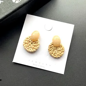 Detail van gevlochten rotan oorbellen met roze hars studs op witte sieraden display kaart