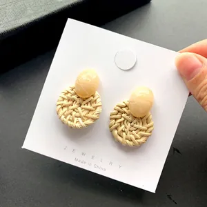 Bohemian geweven rotan oorbellen met crème harsstekkers op een sieradenkaartje