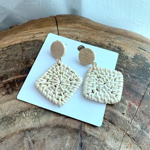 Macro shot of handmade square rattan earrings with wooden studs on a wooden display
