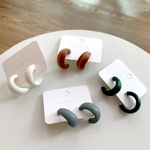 Detailed view of C-shaped wooden hoop earrings in four matte colors on display cards