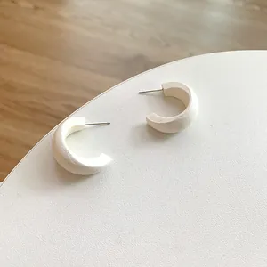 Detailed top view of white C-shaped wooden earrings with a matte texture on white surface