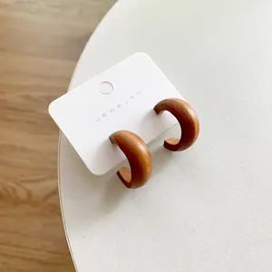 Close-up of brown wooden C-shaped stud earrings with natural wood grain on jewelry card