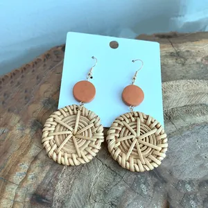 Detailed close-up of handmade bohemian earrings with woven natural rattan and orange discs
