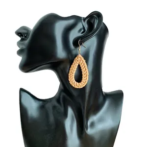 Handmade teardrop wicker earrings with natural straw weaving on a black display model