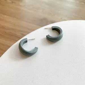 Close-up of matte wood texture C-shaped hoop earrings with gold pins on white stand